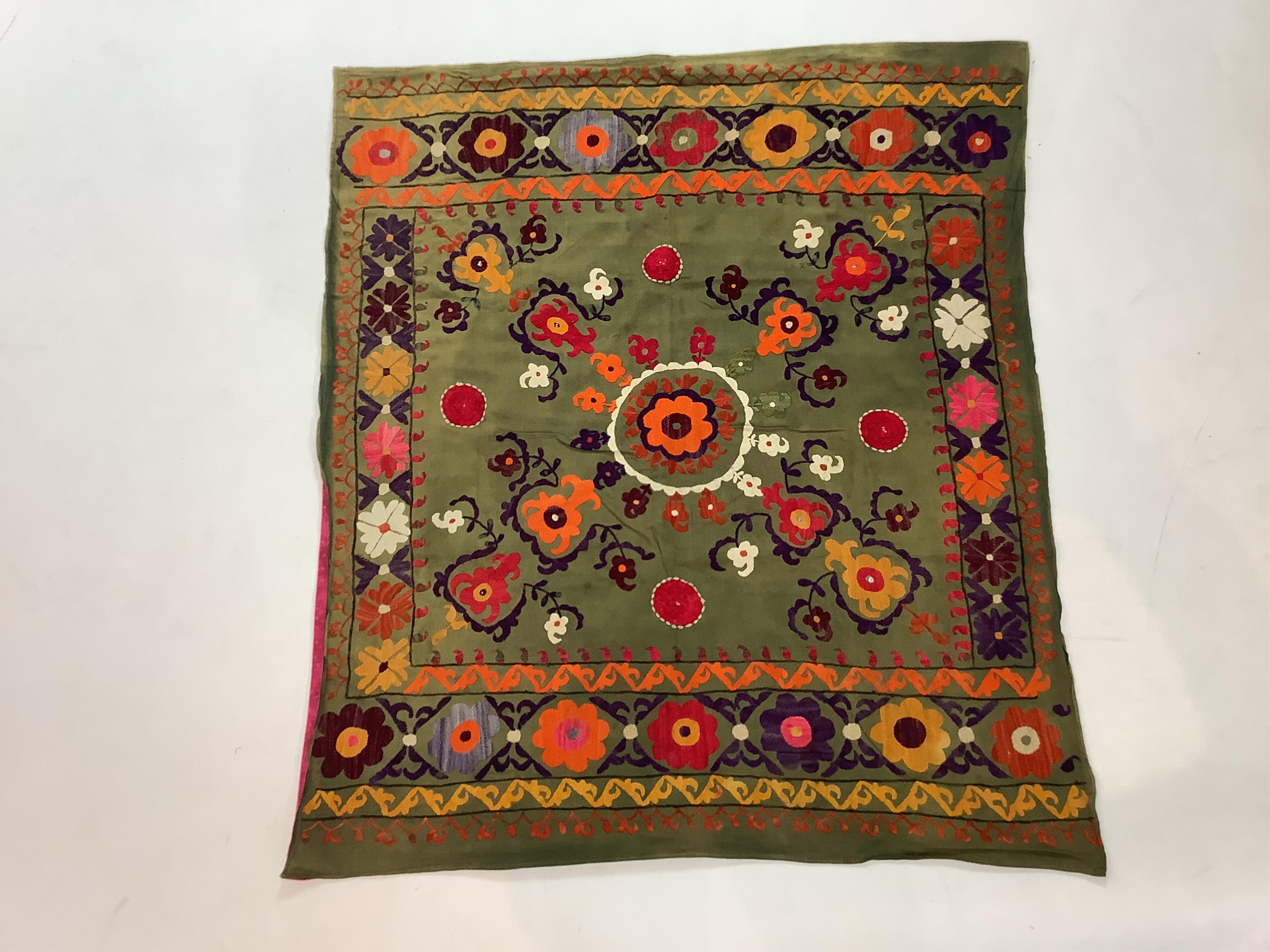 A late 19th early 20th century Suzani table cover. Worked on an olive green cotton in bright polychrome silk threads. Probably from Uzbekistan, made as part of a brides dowry with later lining., 88cm x 98cm. Condition -